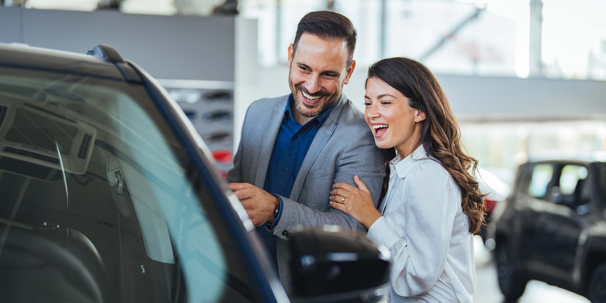 Pareja emocionada explorando un carro en concesionario