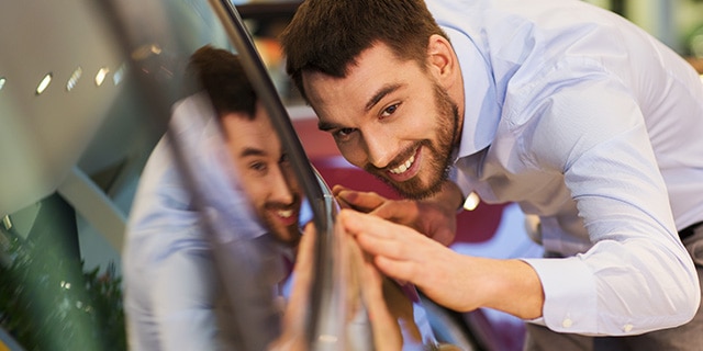Hombre sonriente inspeccionando su carro nuevo en un concesionario Chevrolet.